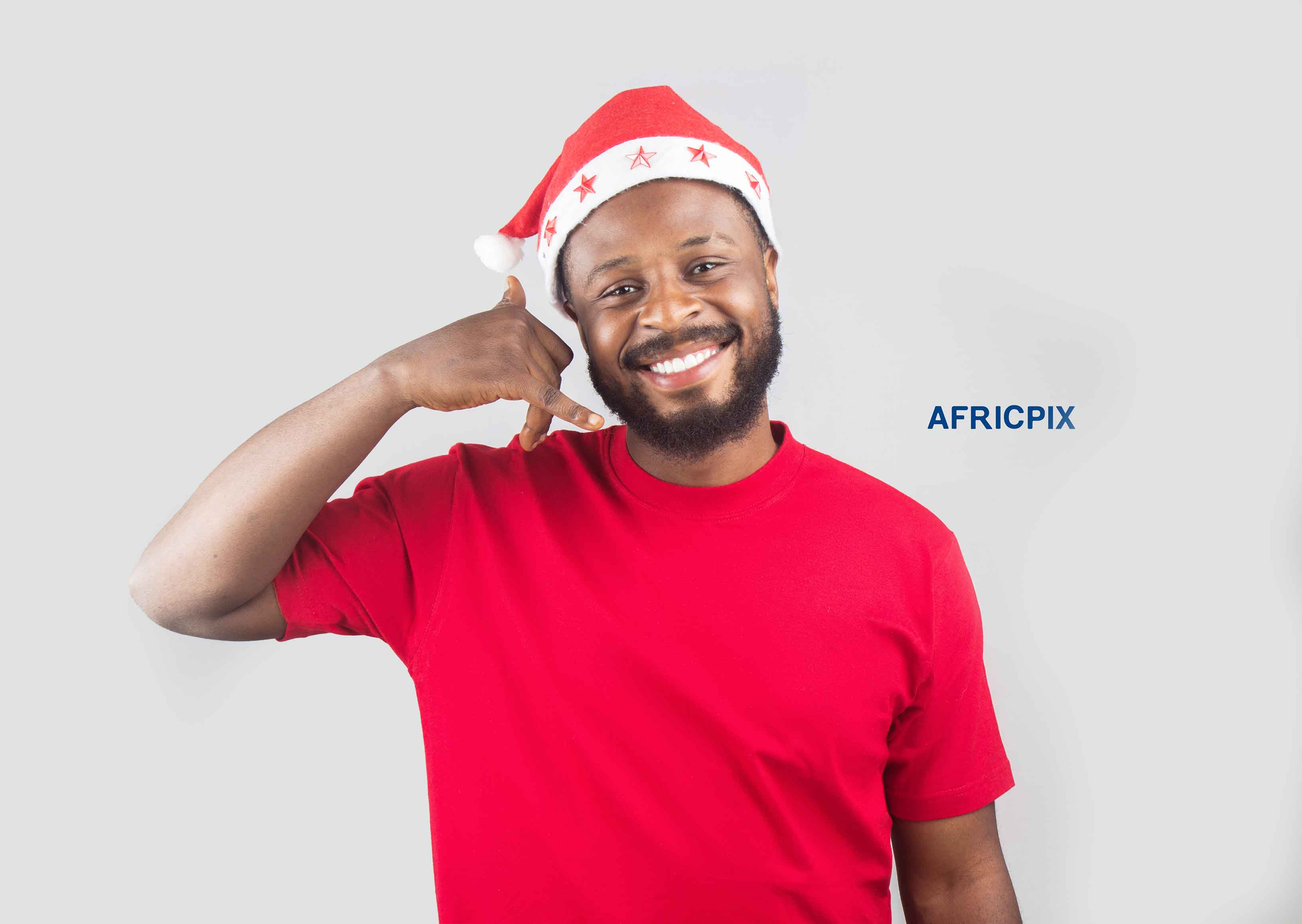 An African Nigerian man wearing a Christmas cap, making a hand gesture like talking on the telephone with his fingers